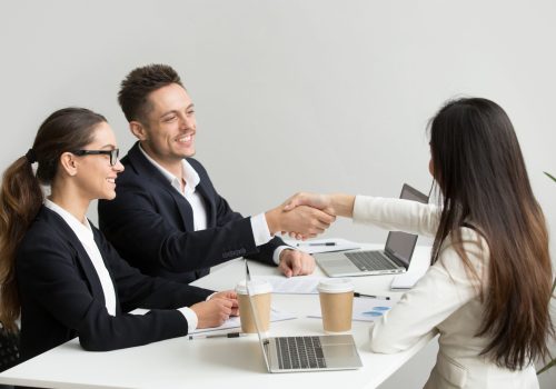 Friendly partners handshaking at group meeting thanking for succ